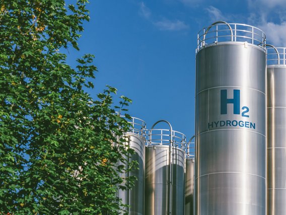Silberne Tanks für die Speicherung von Wasserstoff vor blauem Himmel und Bäumen