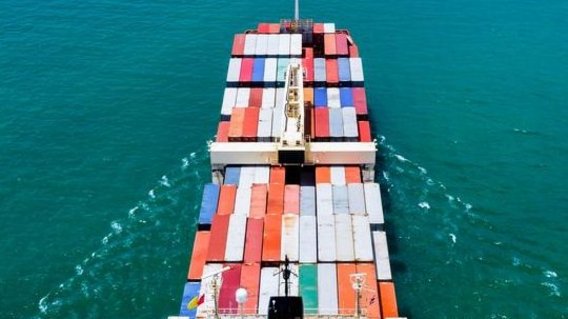 Luftaufnahme eines Containerschiffs auf offenem Meer, beladen mit bunten Frachtcontainern.