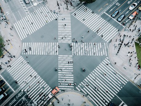 Luftaufnahme einer belebten Fußgänger-Kreuzung mit Zebrastreifen in alle Richtungen in einer Großstadt.